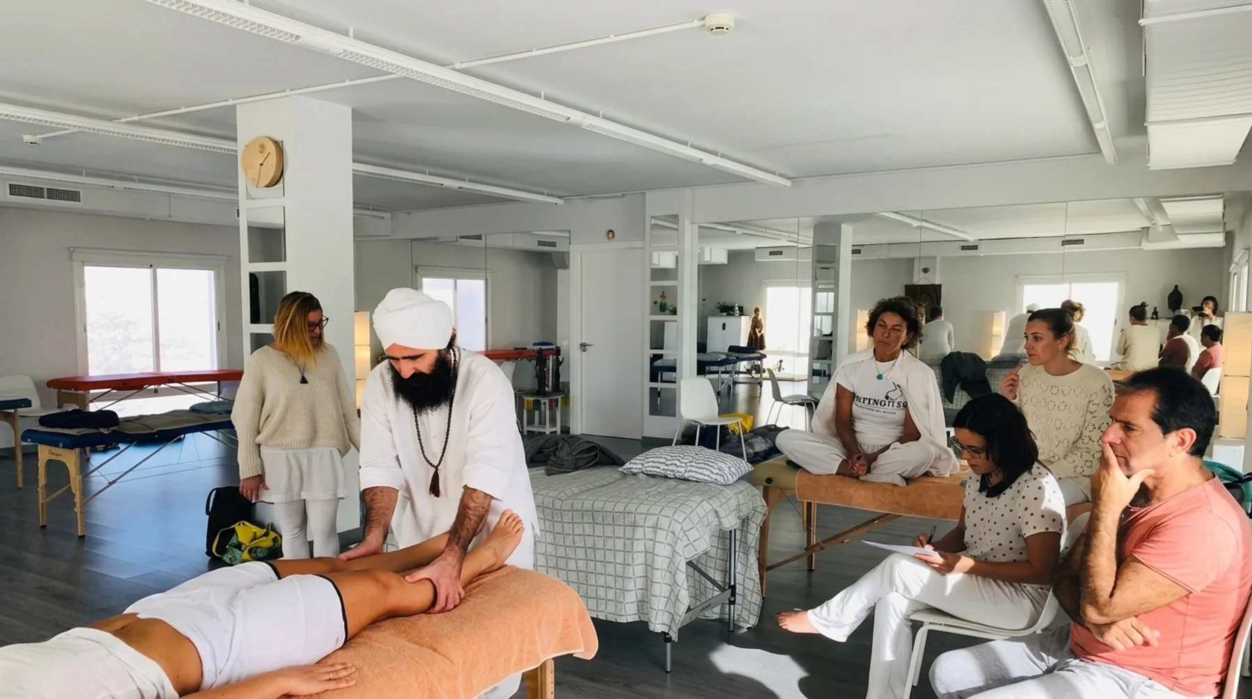 Lakhmi Chand aplicando un tratamiento de masaje yóguico durante una clase práctica, con alumnos observando y tomando apuntes